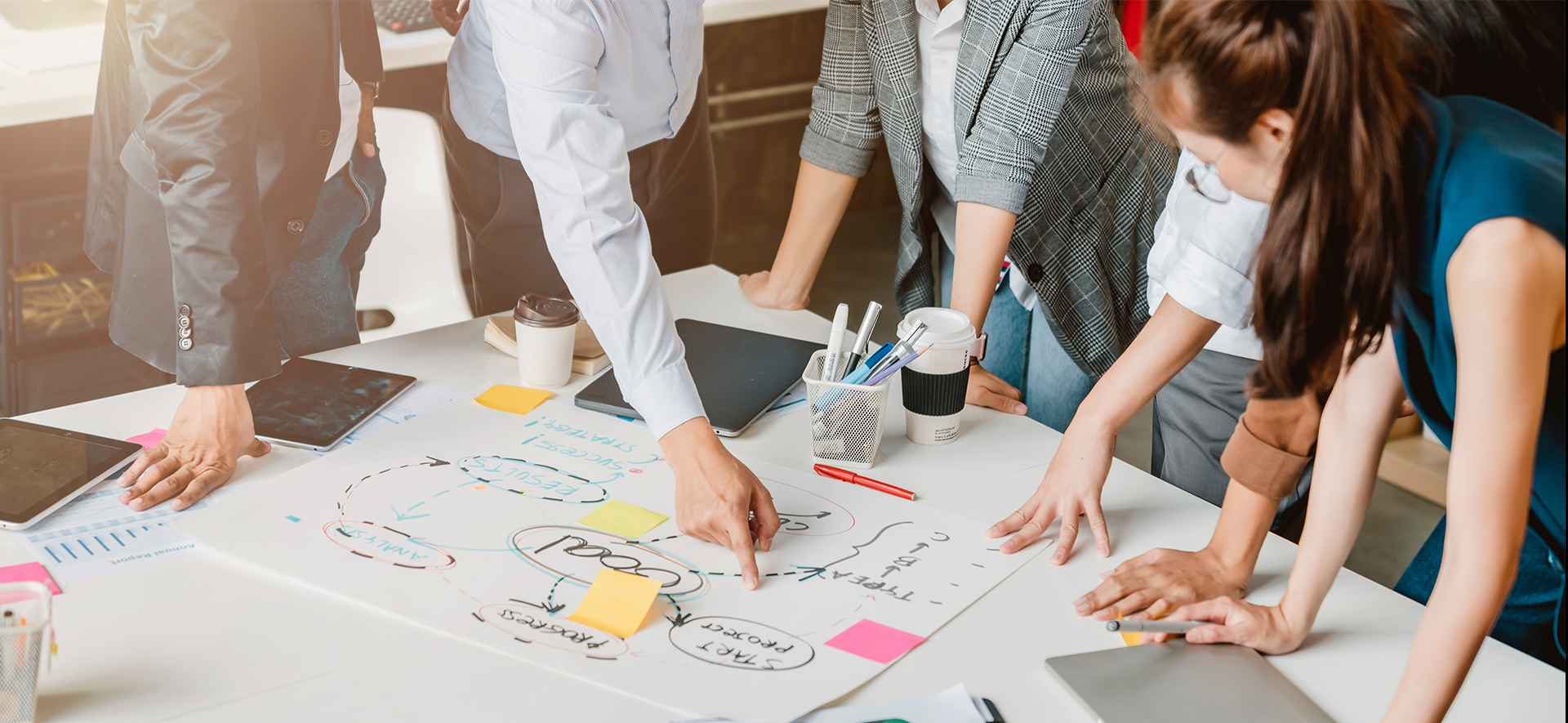 Grupa osób stojąca nad stołem, na którym rozłożone są dokumenty