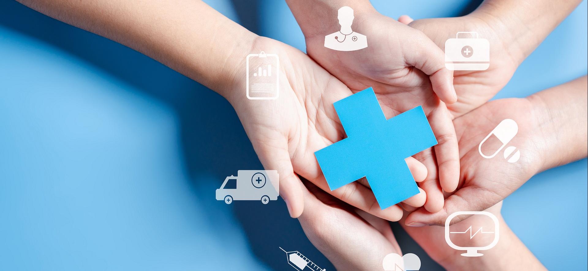dłonie trzymające papierowy niebieski krzyż symbolizujący ochronę zdrowia, wokół multimedialne e-usługi 