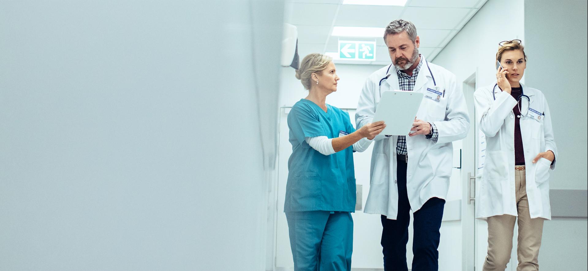 pielęgniarka, lekarz i lekarka rozmawiają, stojąc na korytarzu