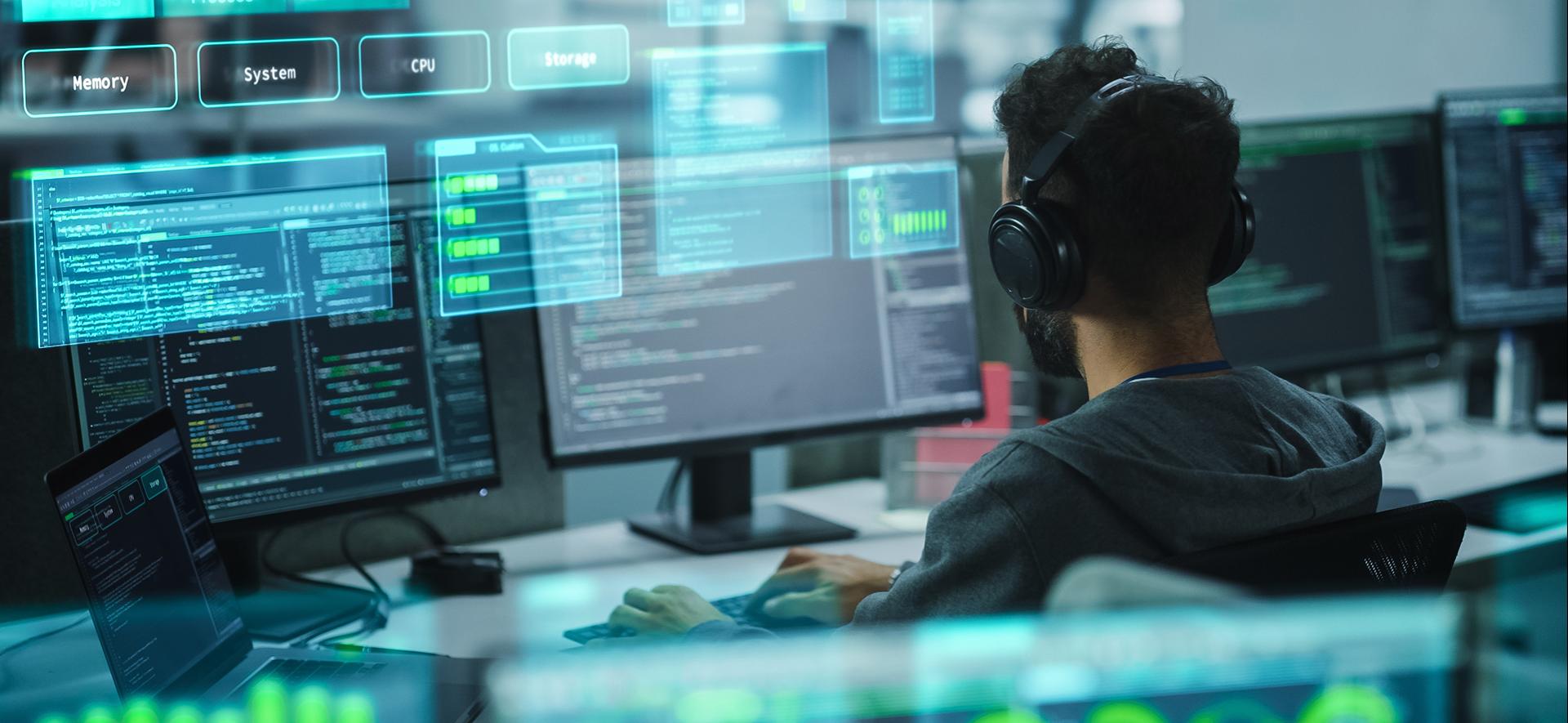 osoba siedzi tyłem przed ekranami