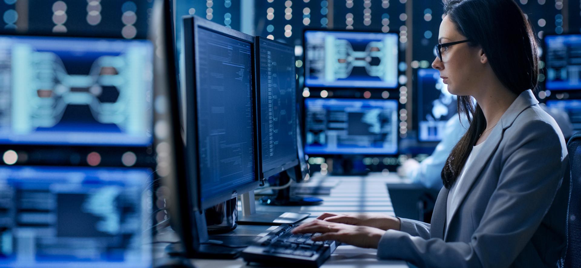 Kobieta pracująca przy komputerze otoczona monitorami
