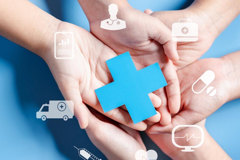 dłonie trzymające papierowy niebieski krzyż symbolizujący ochronę zdrowia, wokół multimedialne e-usługi 