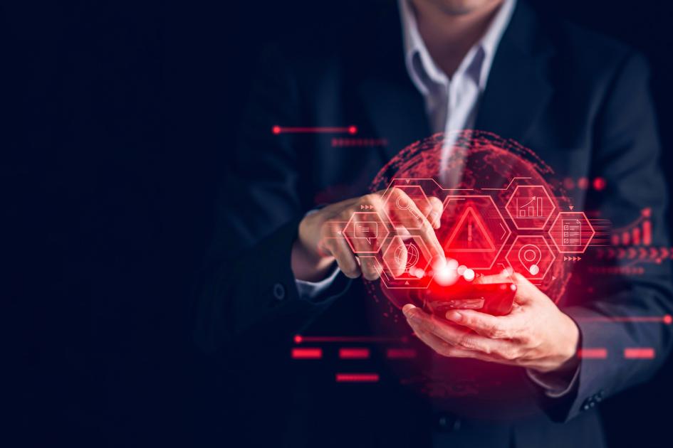 w tle widoczna jest osoba w garniturze, na pierwszym tle widać ręce trzymające telefon , a z niego unszą się czerwone ikony