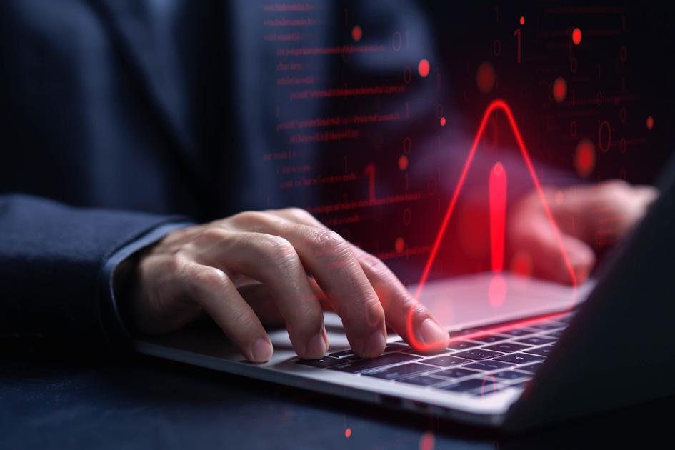 ręce na klawiaturze laptopa i z laptopa wyłania się czerwony, świecący wykrzyknik w trójkącie