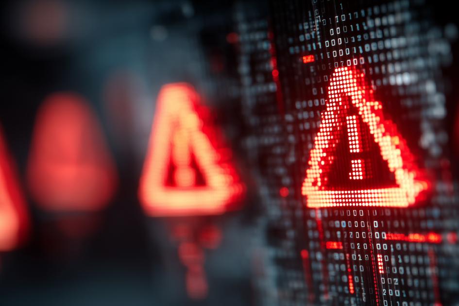 czerwony trójkąt z wykrzyknikiem w środku unosi się nad klawiaturą laptopa