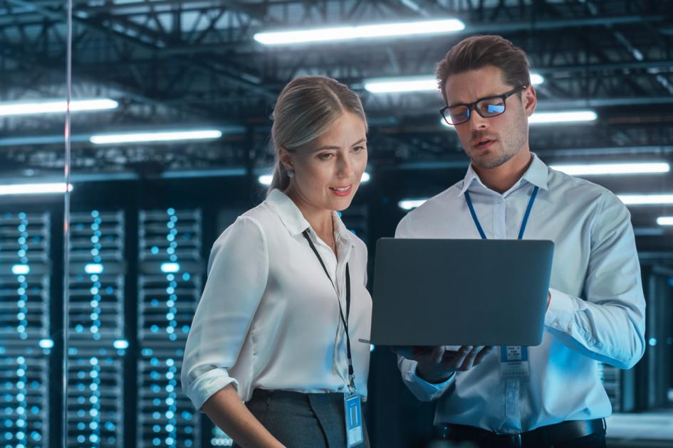 kobieta i mężczyzna ubrani w białe koszule patrzą na ekran laptopa